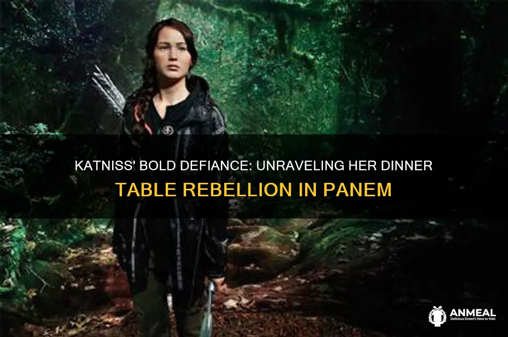 how does katniss show defiance at the dinner table